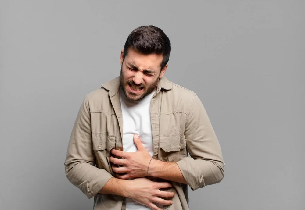 Hombre de pie sujetándose el abdomen con gesto de dolor por problemas digestivos y reflujo.