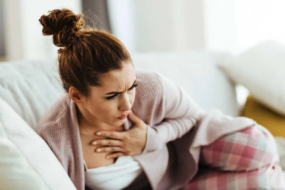 Mujer sentada en un sofá expresando dolor y presión en el pecho, síntoma común del reflujo gastroesofágico.